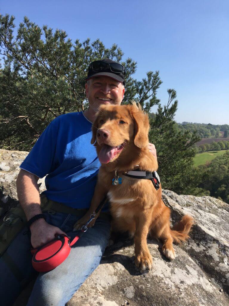 Man and Duck Toller retriever sat on a rock