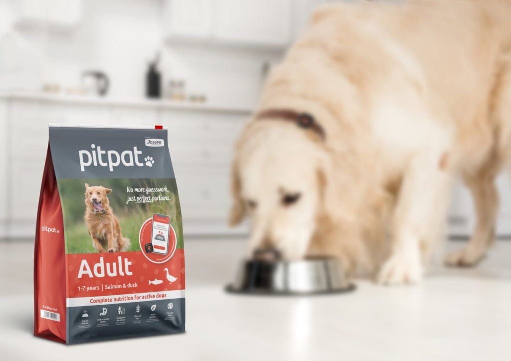 A bag of PitPat food with a Golden Retriever eating in the background