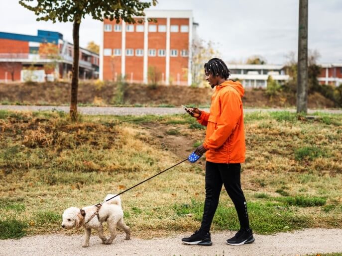 man in orange jacket walking dog in urban area
